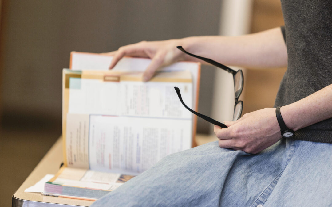"Person reviewing adoption paperwork and holding a pair of glasses, pausing mid-review at a table.